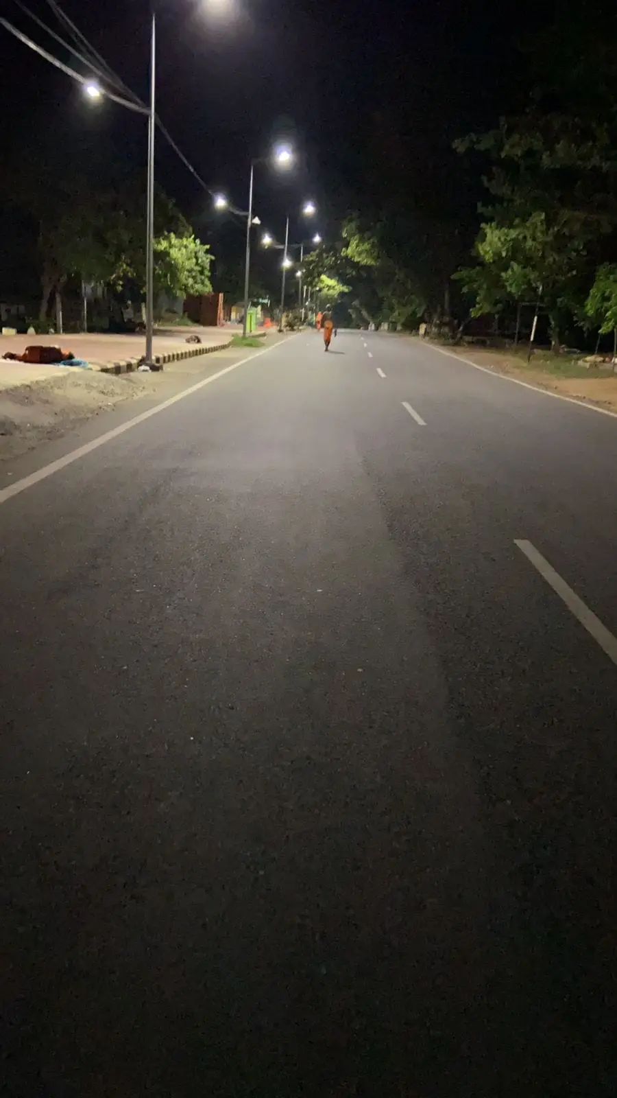 A lone pilgrim in saffron walking the lit Girivalam road at night