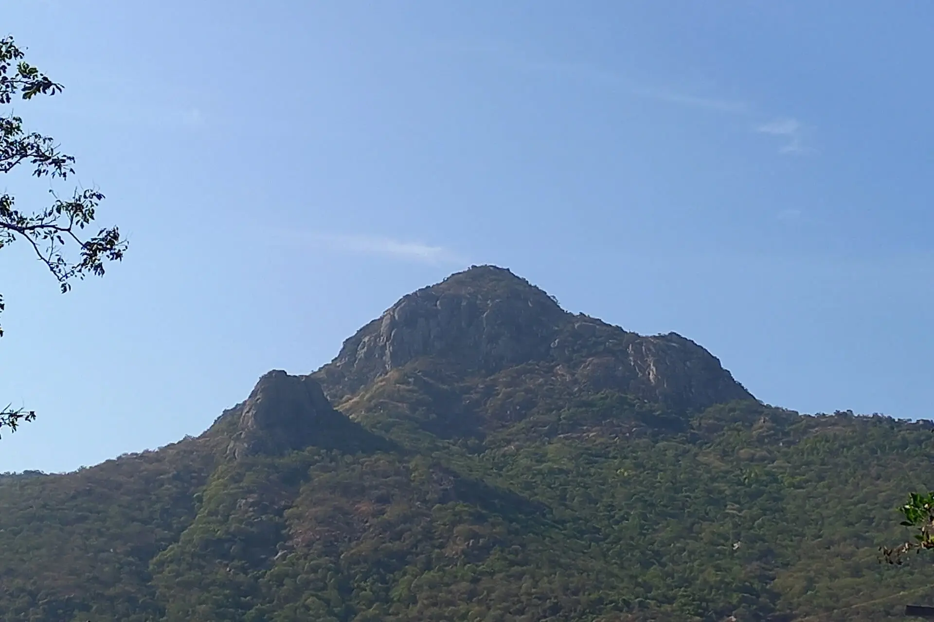 The rocky summit of Arunachala hill against a clear blue sky, seen from near the Vayu Lingam on the Girivalam path