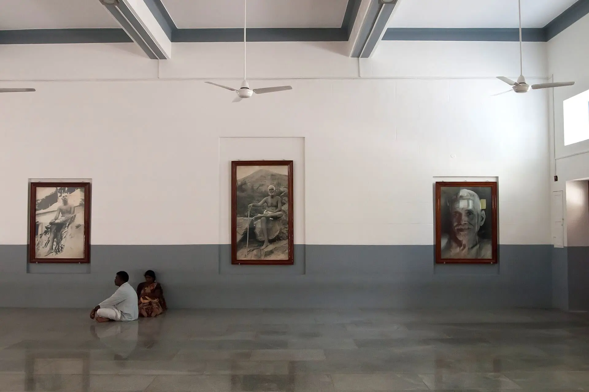 Devotees sitting quietly in a meditation hall at Sri Ramanasramam beneath portraits of Ramana Maharshi